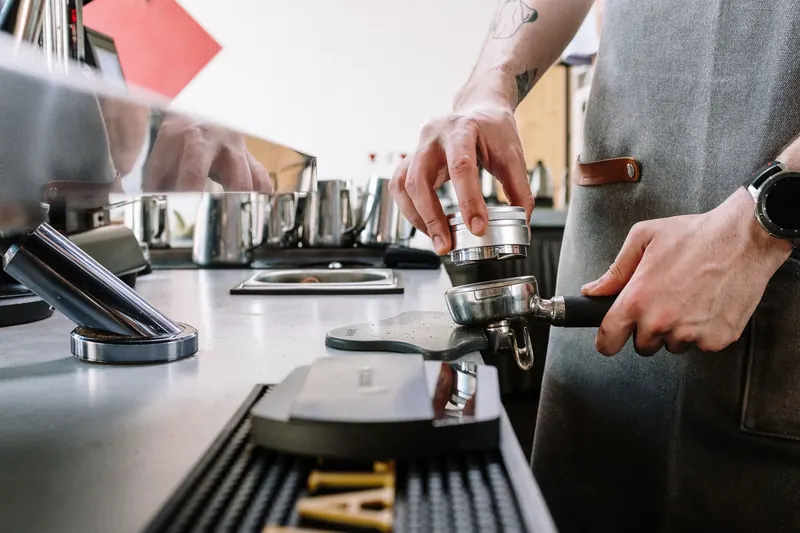 Close-up of a barista tamping coffee grounds with a portafilter in a café setting