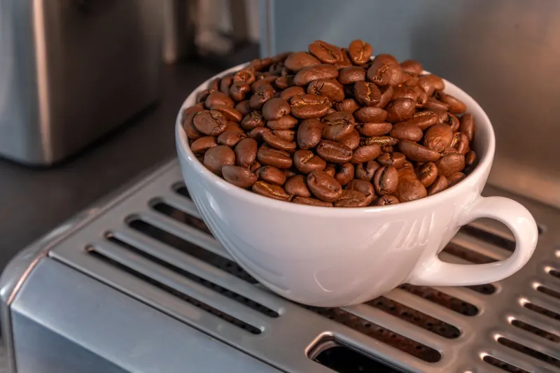 A close-up of aromatic roasted coffee beans piled in a white cup on a metal surface
