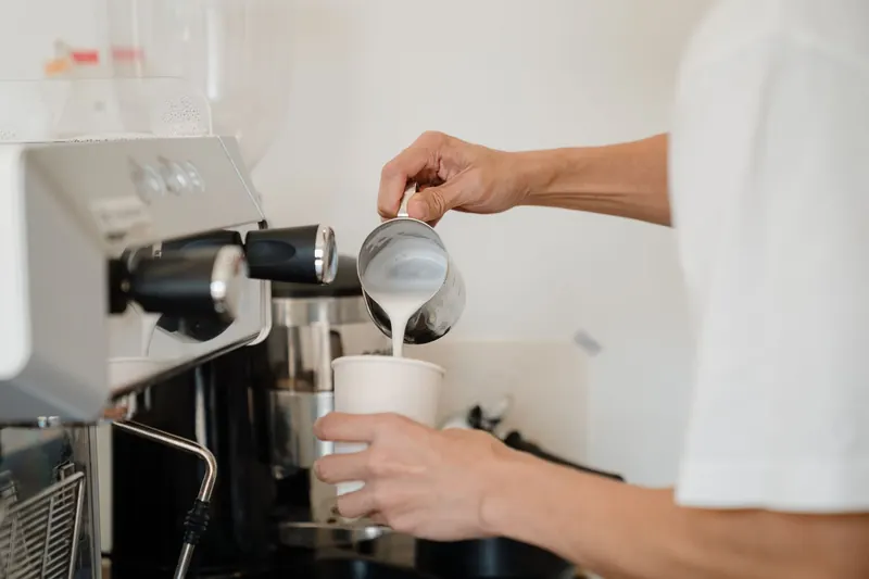 Barista carefully pouring steamed milk into a cup to create a delicious coffee beverage at a café